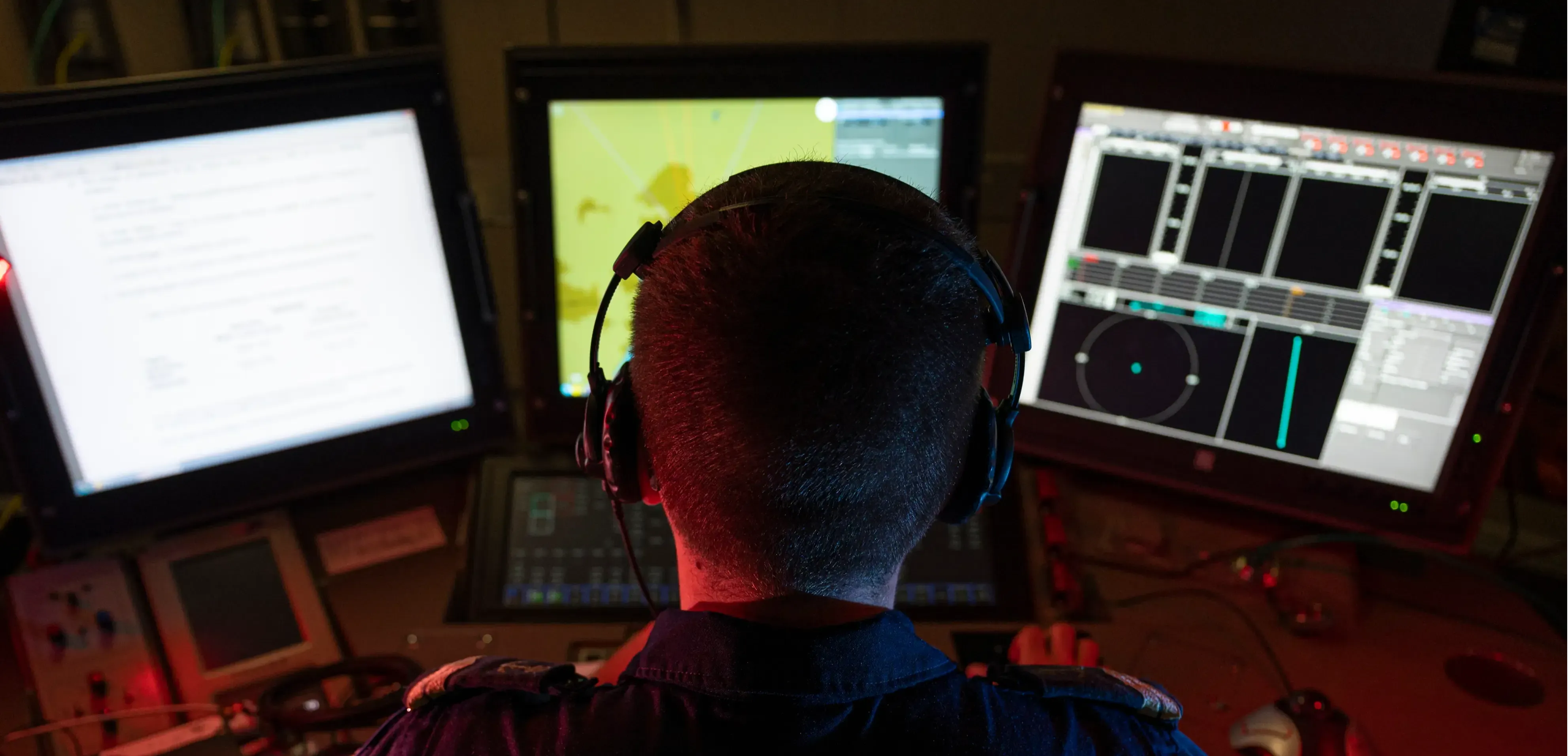 Un marin de spécialité detecteur anti sous-marins photographié de dos à son poste de contrôle composé de trois écrans d'ordinateur