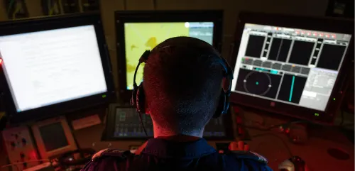 Un marin de spécialité detecteur anti sous-marins photographié de dos à son poste de contrôle composé de trois écrans d'ordinateur