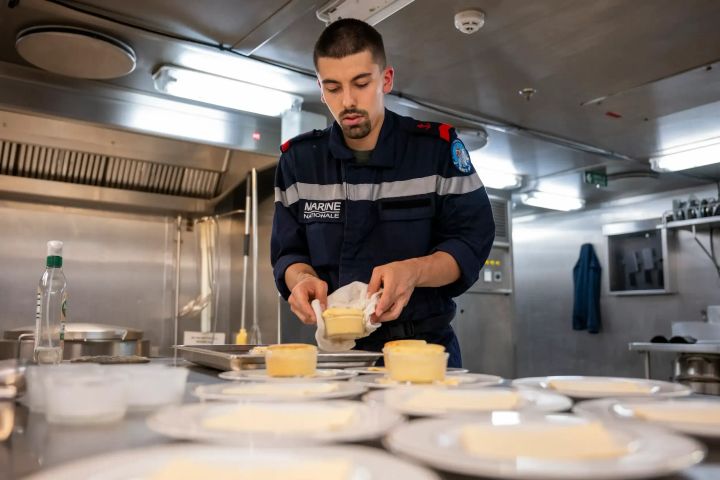Un matelot cuisinier en train de préparer le repas pour l'équipage, dans la cuisine d'un navire.