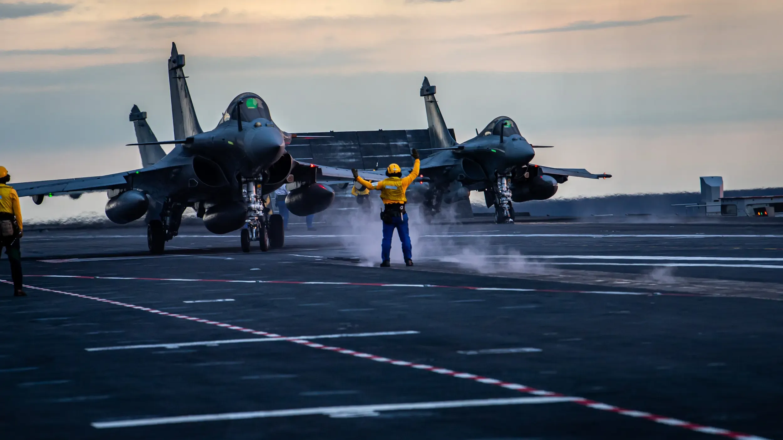 Deux rafales parés au décollage sur le pont d'un porte avion et un opérateur de pont d'envol leur donnant le signal