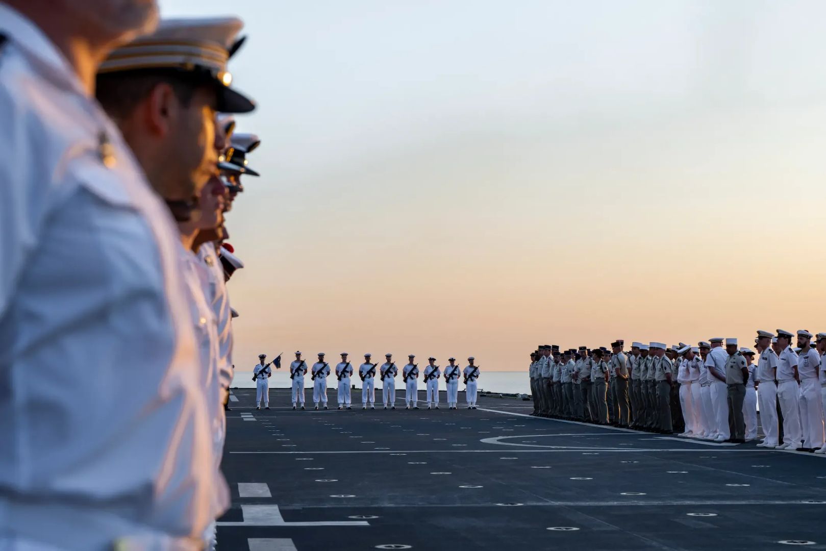 une cérémonie de la marine nationale sur le pont d'un navire au levé du soleil, les marins sont en uniforme blanc.