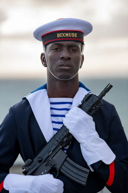 Le portrait d'un matelot de la Marine nationale, en uniforme de cérémonie avec gants blancs et arme de cérémonie.