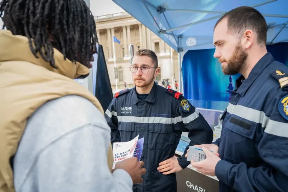 Des marins spécialistes de la force sous-marine en discussion avec un jeune sur un stand d'événement de recrutement. 