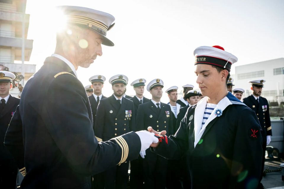 Une cérémonie de remise de galons. Un commandant de la marine nationale remet les galons à un matelot devant les troupes alignées en rang et tenues de cérémonies.