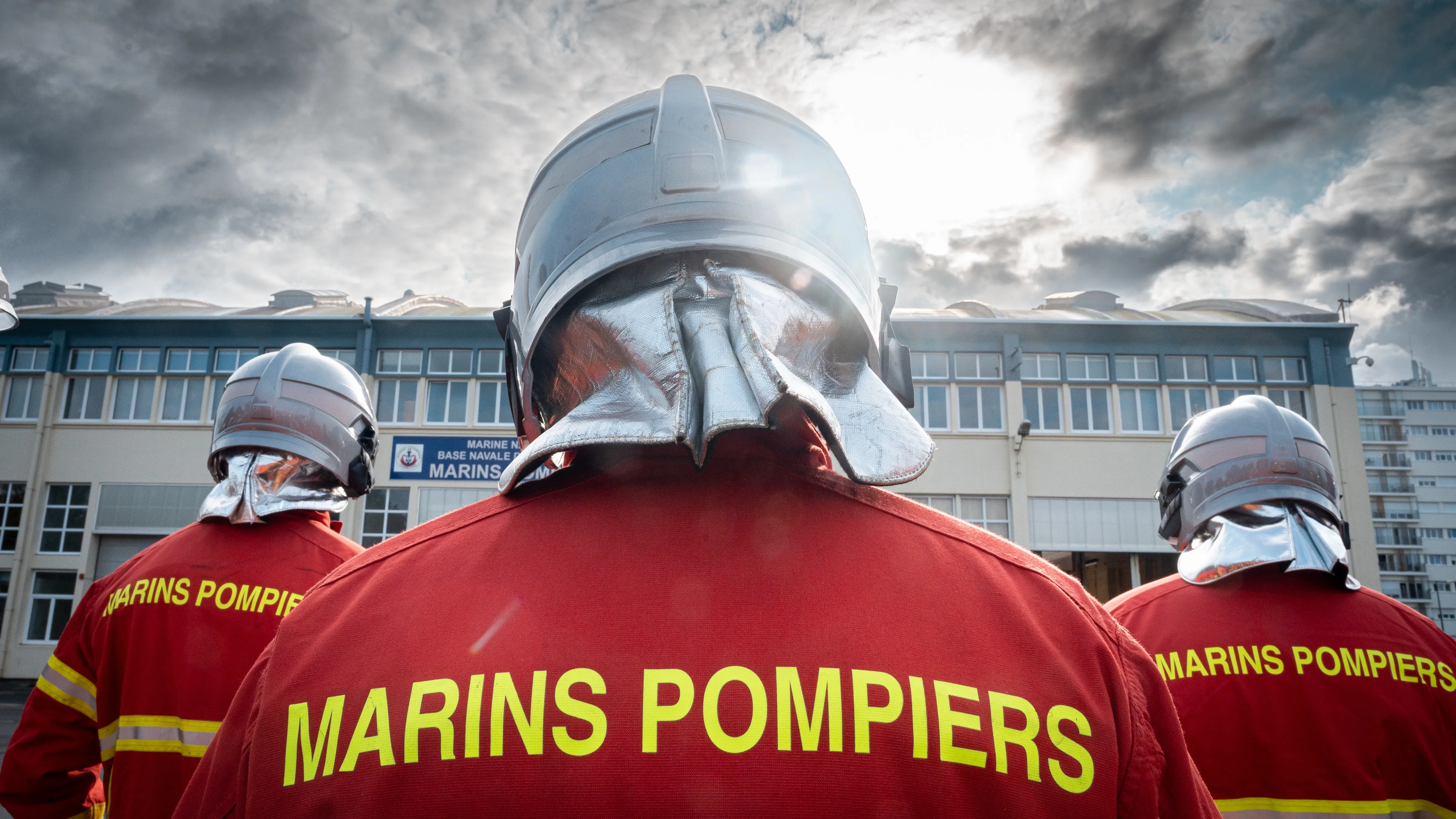 Trois marins pompiers de dos en uniforme rouge avec un casque argenté