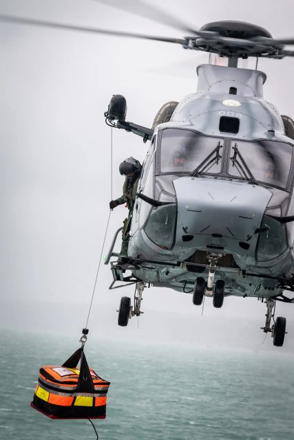 Un hélicoptère gris de la marine nationale, en plein exercice de secourisme, l'image montre l'hélicoptère en train d'apporter un sac de matériel médical.