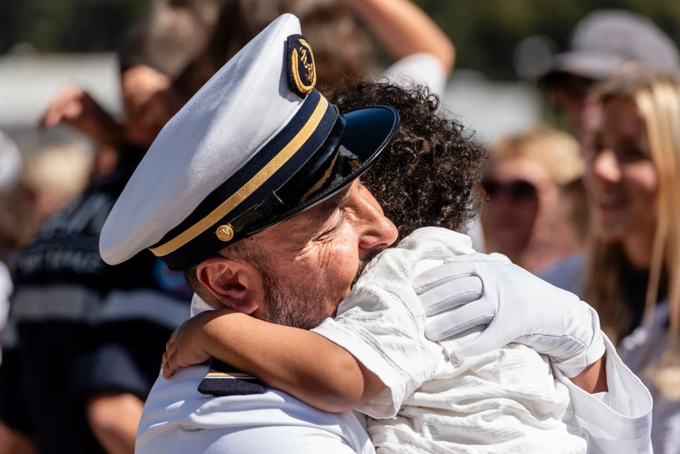 Retrouvaille d'un père marin et de son petit enfant, le père est en tenue de cérémonie et enlace son enfant.