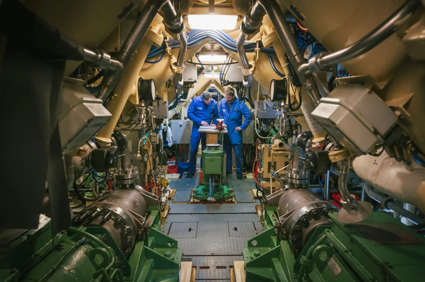 Des atomiciens en tenue bleue de travail en train de travailler dans la salle des machines d'un navire à propulsion nucléaire.