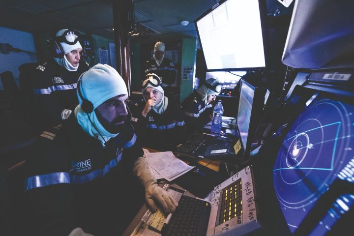 Un groupe de marins en tenue de service en train d'analyser des écrans de contrôle pour la navigation d'un navire