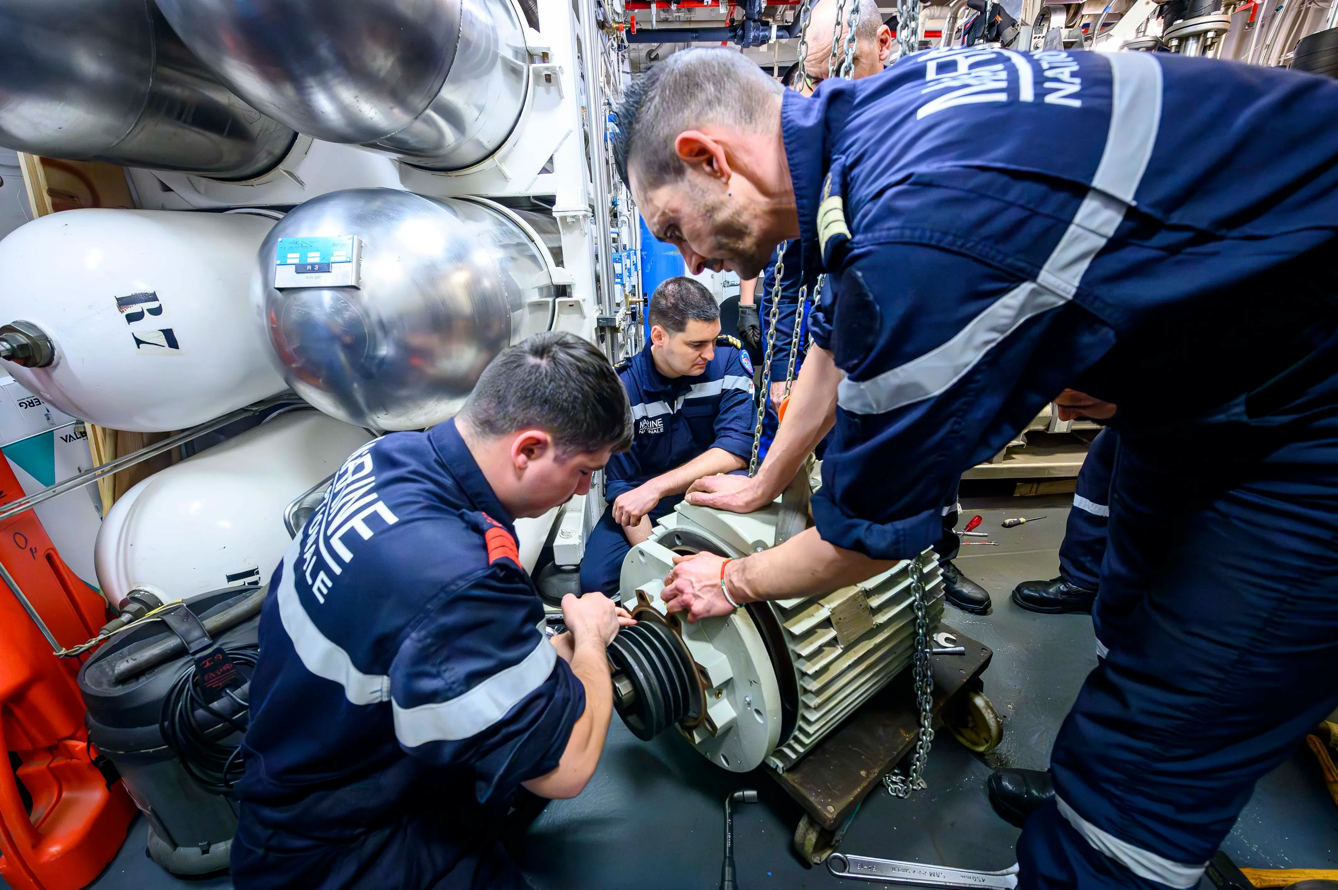 Une équipe de marins opérateur industriel en atelier naval, en train de travailler sur une pièce mécanique