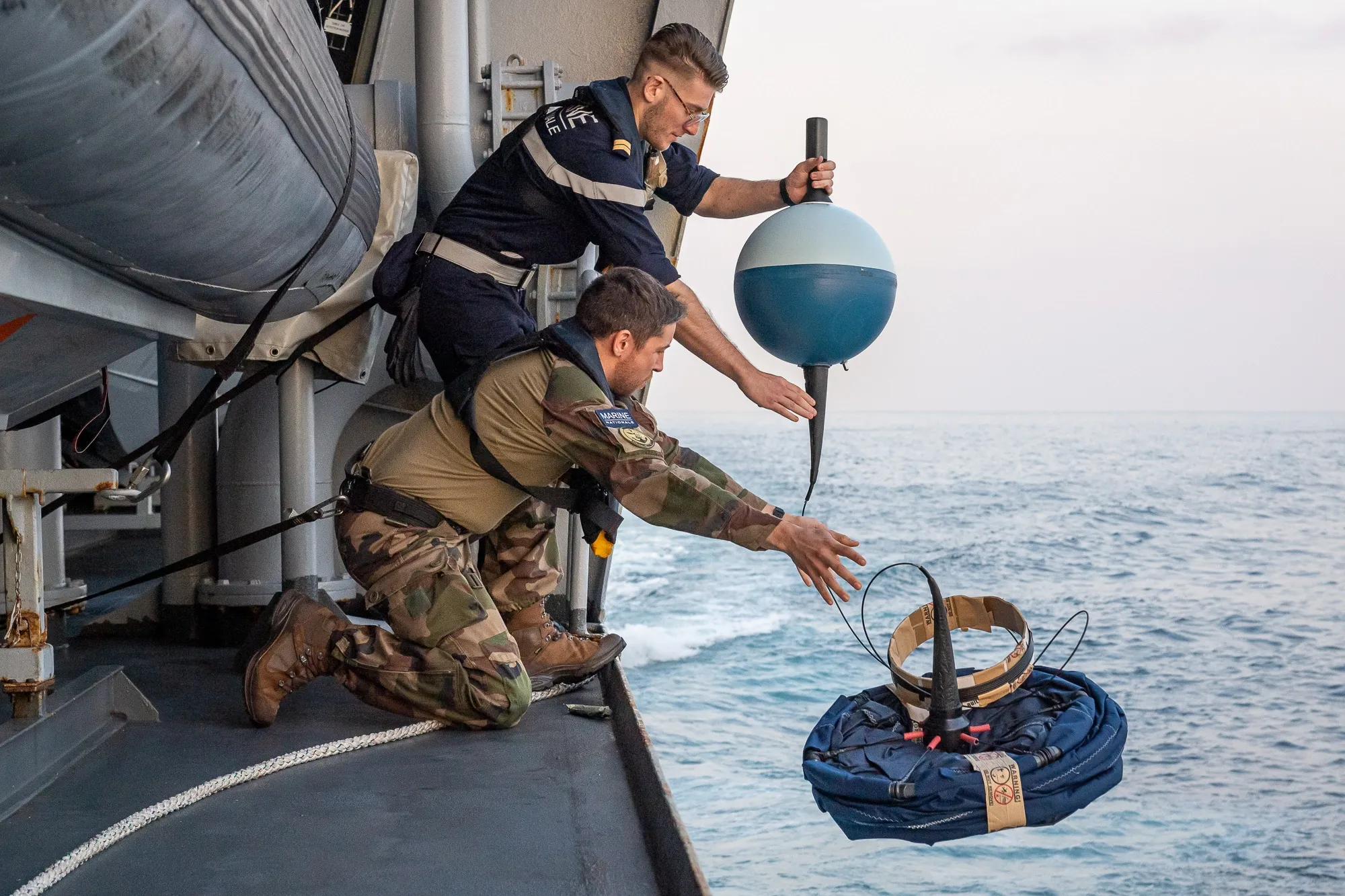 Deux marins météorologistes-océanographes en train de mettre une bouée à la mer pour relever des données