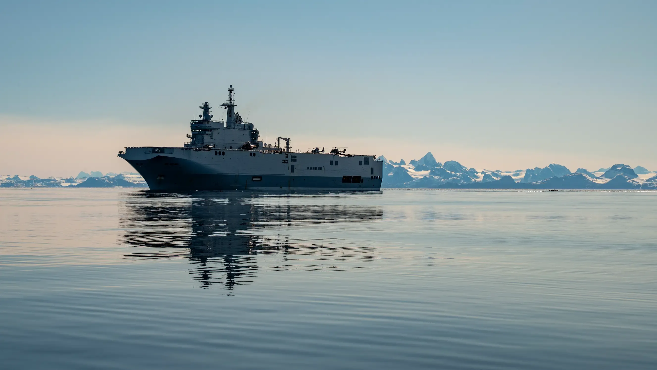 Un navire de la marine nationale naviguant sur les eaux calmes du Groenland, en fond on peut apercevoir des montages enneigées.