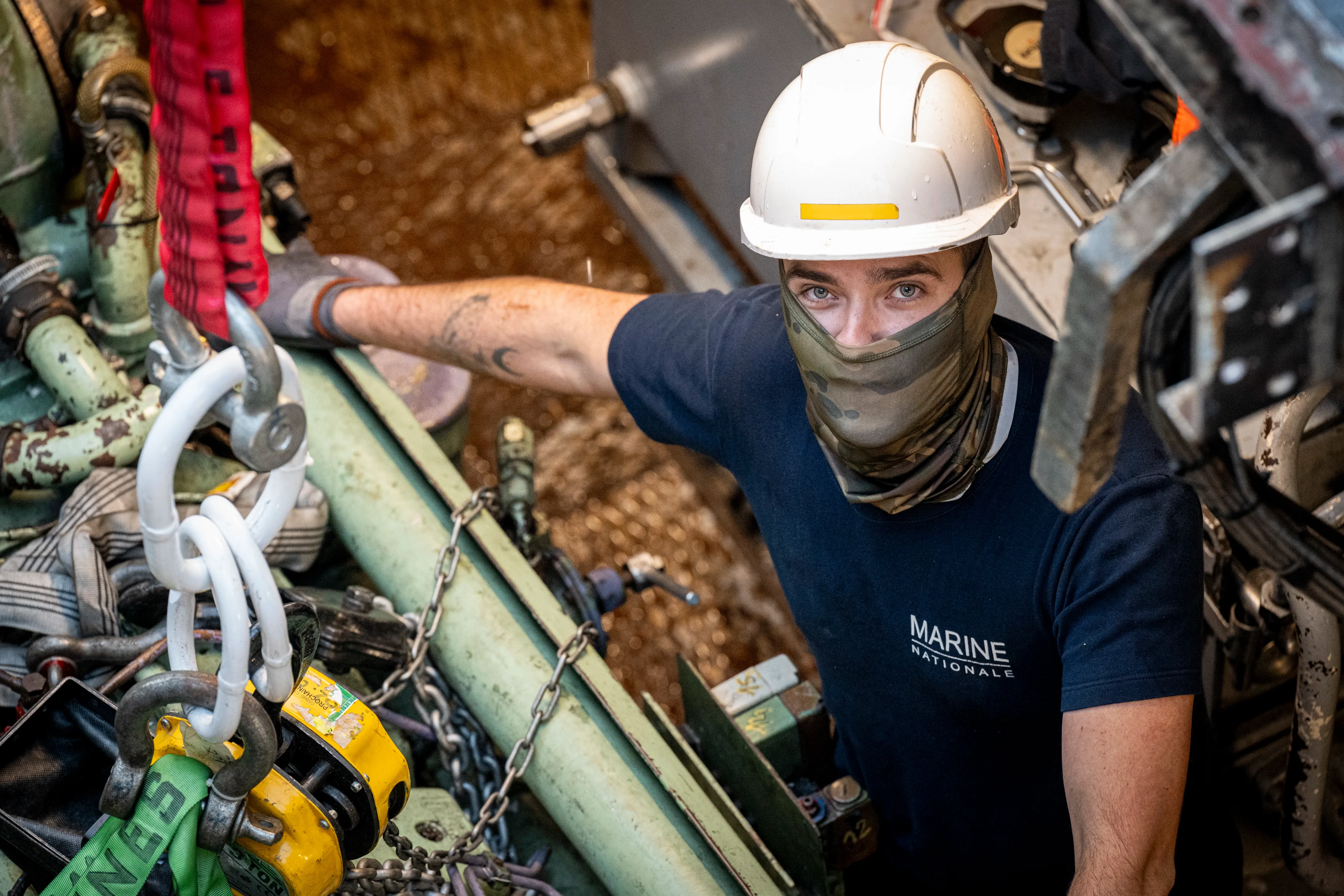 Un technicien de maintenance navale avec un casque blanc travaillant dans les machineries. 