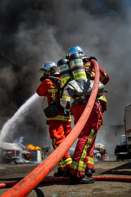 Deux marins pompiers en train de porter une lance à incendie et tentant d'éteindre un feu dans un milieu urbain.