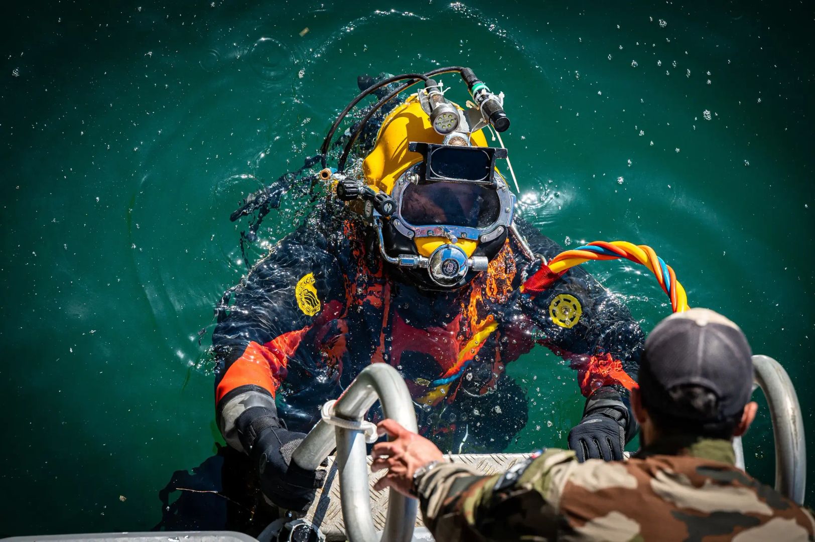 Un instructeur de plongée en treillis, donnant des indications à un élève apprenant la plongée et en scaphandre de plongée.