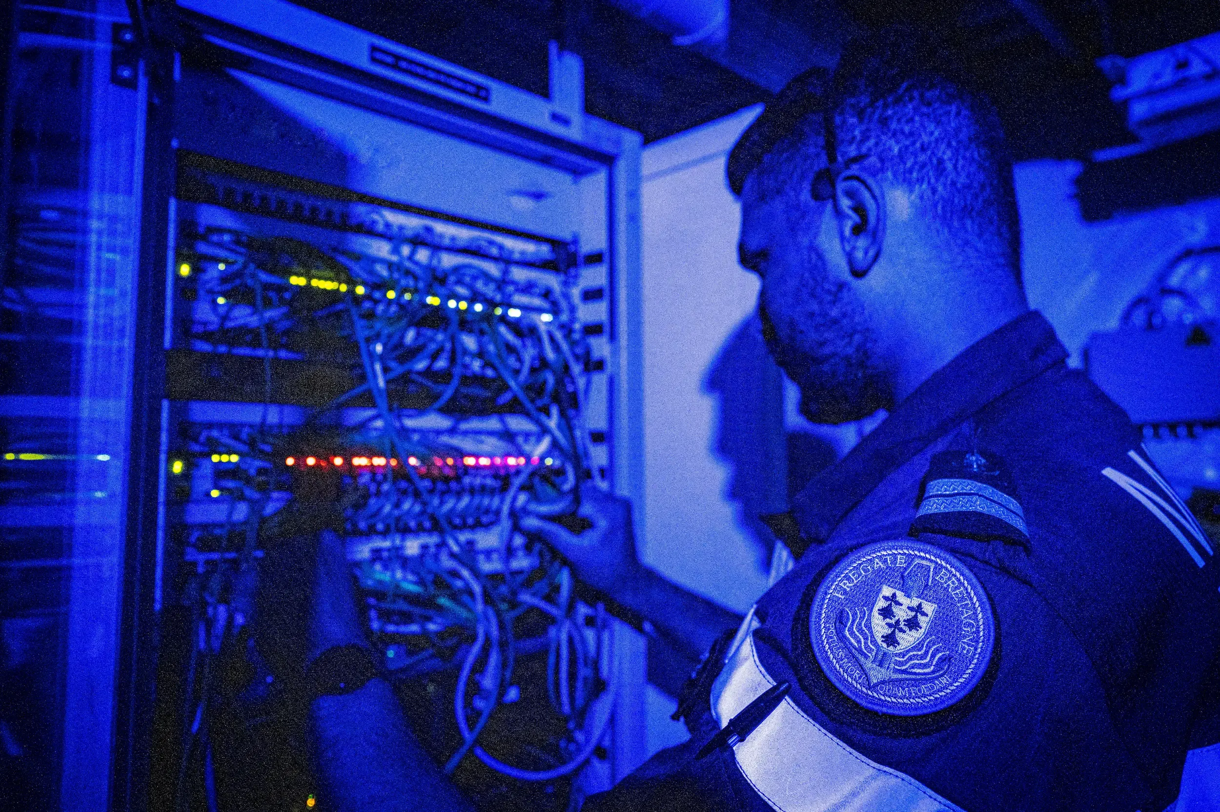 un tehcnicien de la marine en train de travailler sur le tableau d'un réseau de télécommunication.
