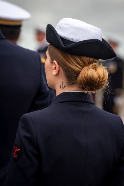 Une matelot de la Marine nationale, vue de dos, en uniforme, avec un chignon et un tatouage discret d'ancre au niveau du cou.
