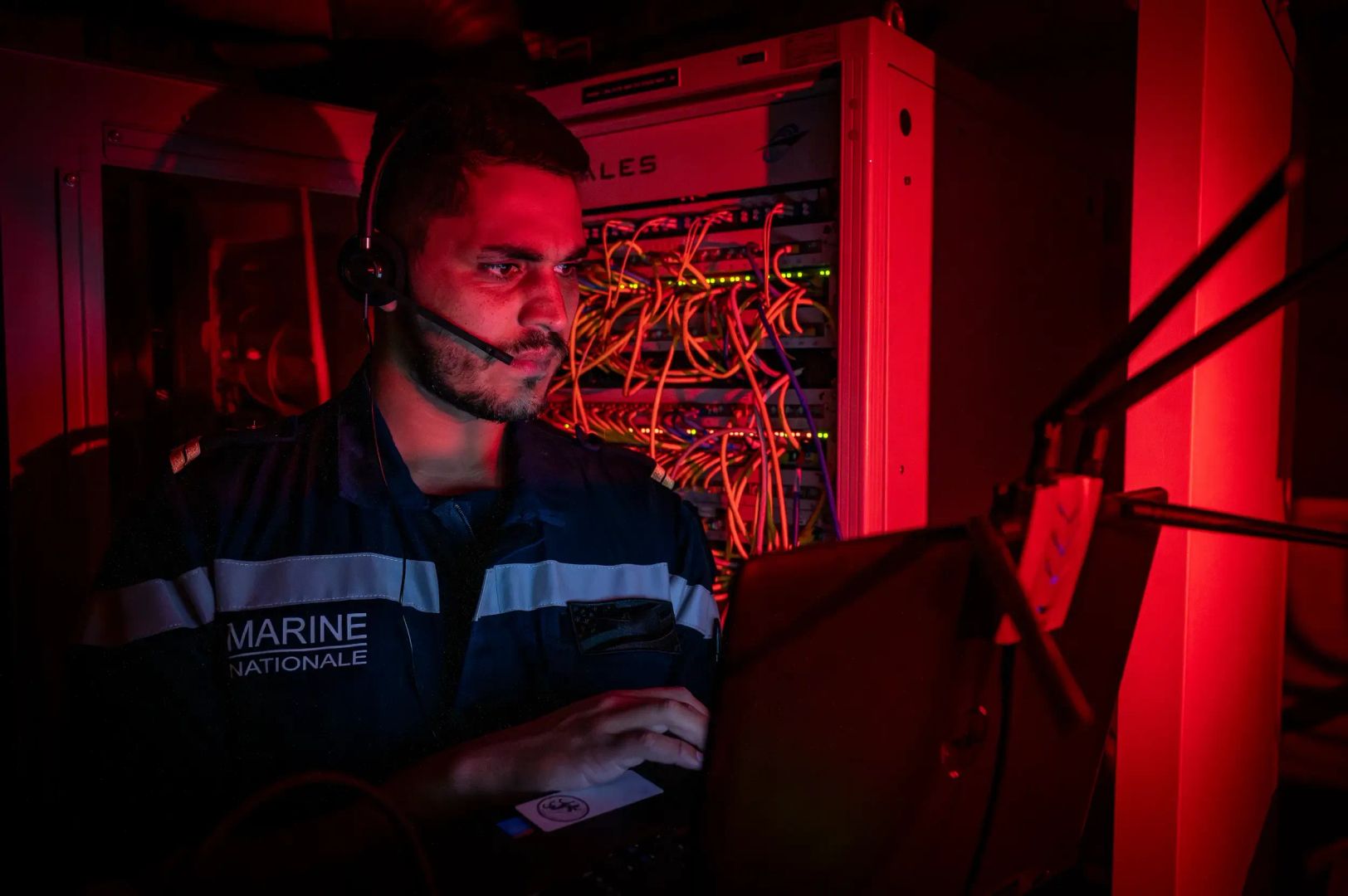 Un technicien réseaux de la marine nationale en train de travailler sur les équipements du réseau d'un navire.