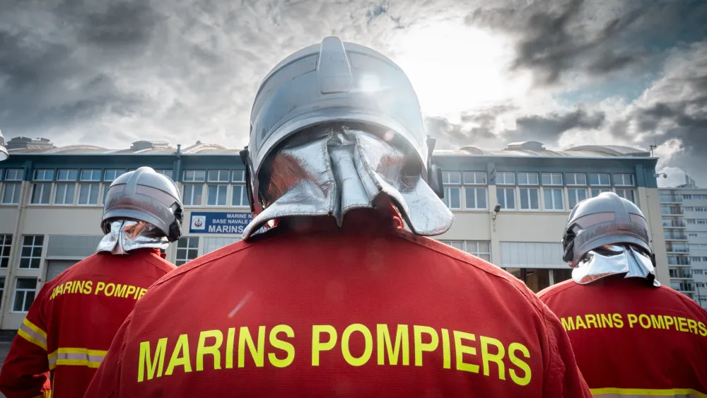 Trois marins pompiers de dos en uniforme rouge avec un casque argenté