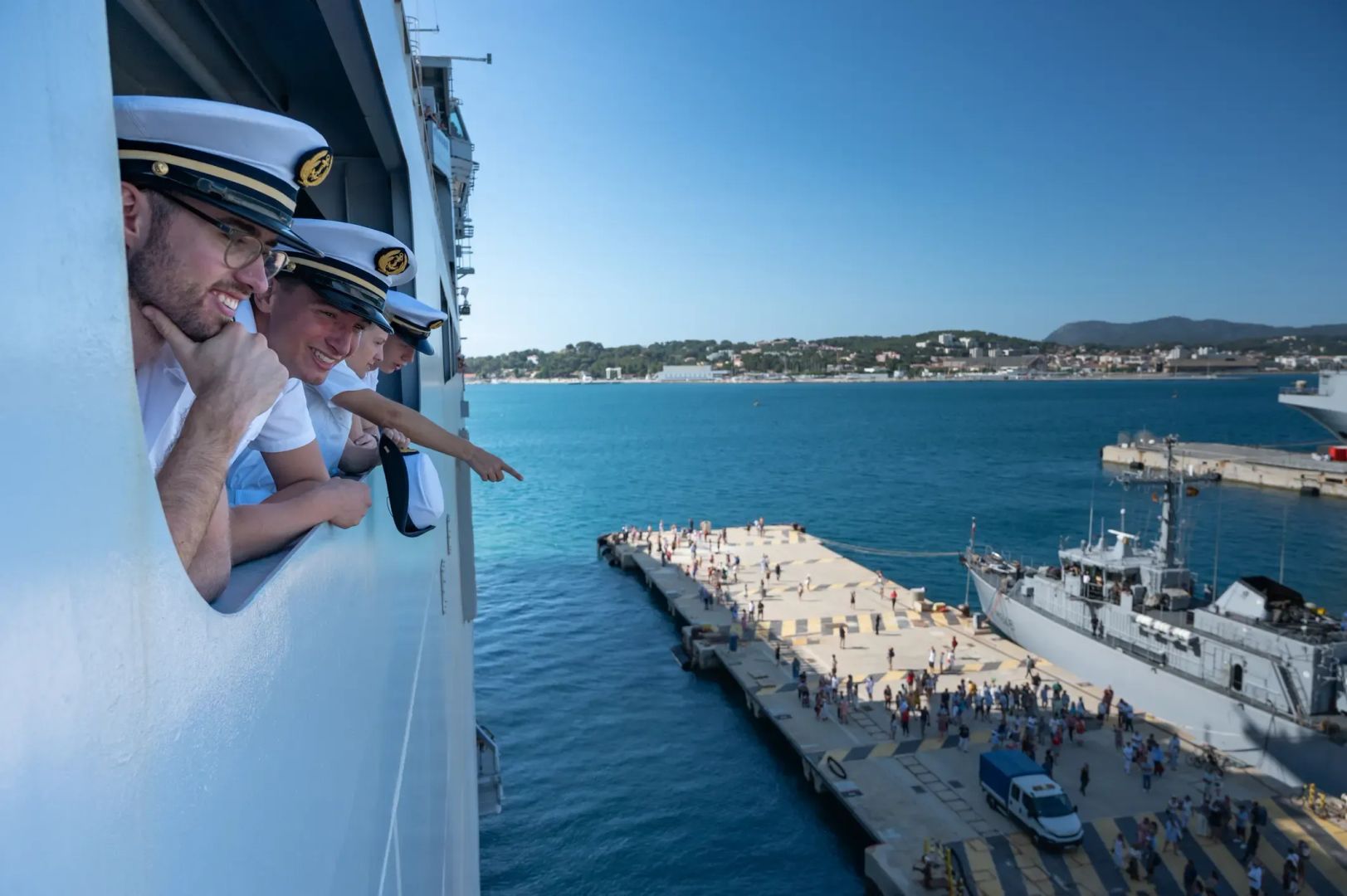 photographie de marins sur un navire de retour d'une mission, regardant les proches et familles les attendant sur le quai.