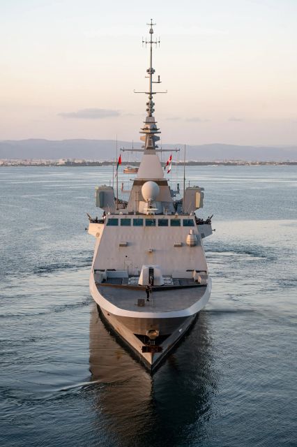 Une frégate de la marine française naviguant face à l'objectif sur une mer calme au levé du soleil.