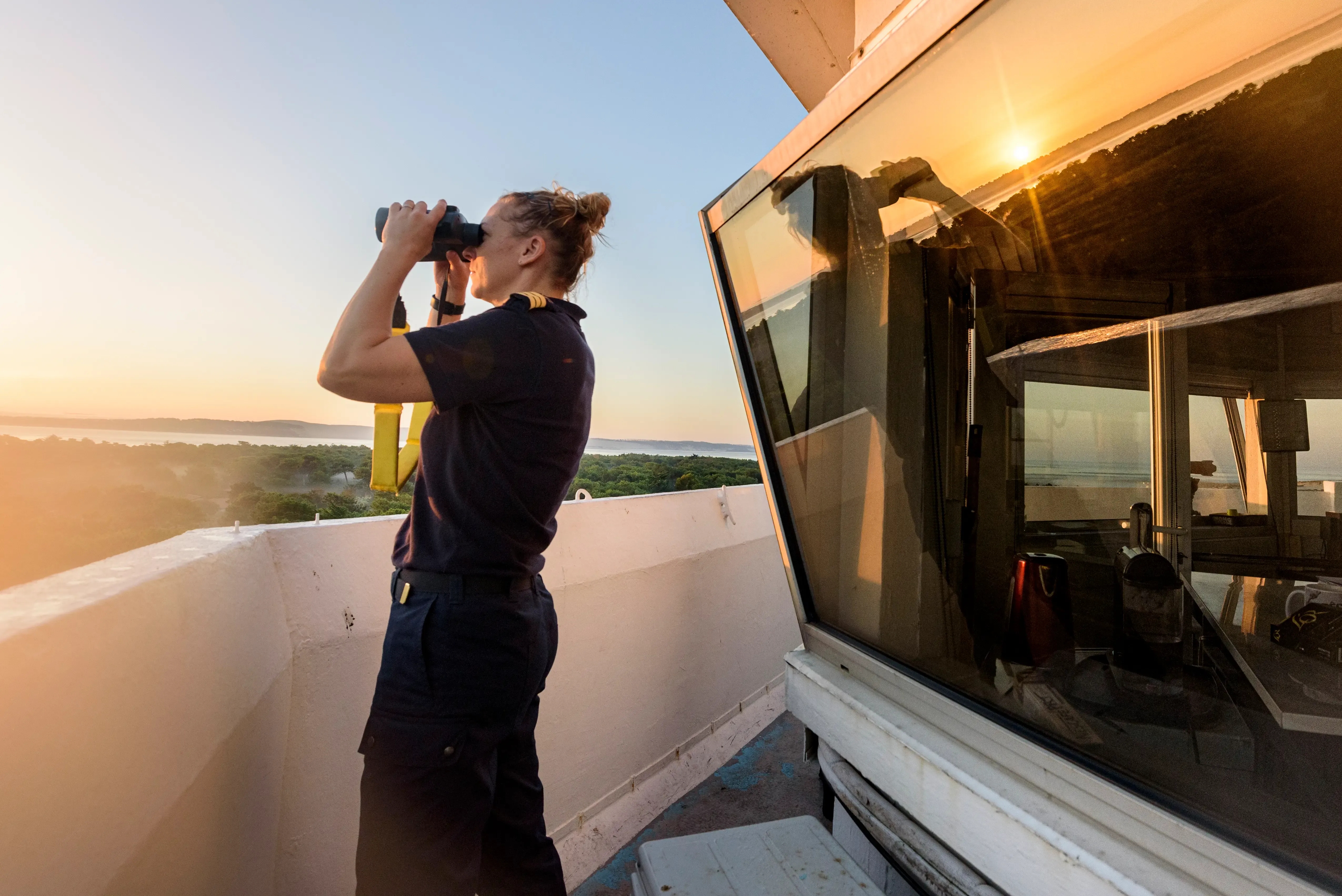 Une technicienne sémaphoriste en train de surveiller la mer avec ses jumelles lors d'un coucher de soleil
